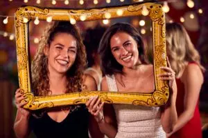 Female Friends Having Fun Posing With Photo Booth Photo Frame At Party In Bar